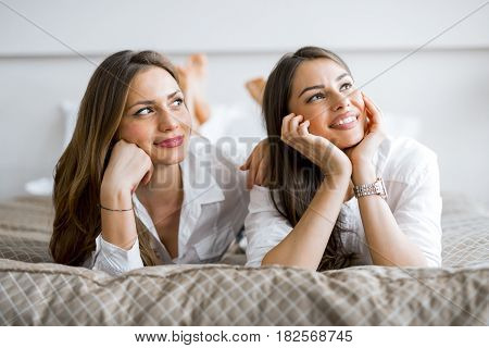 Two beautiful girls talking and smiling while lying on a luxorious bed