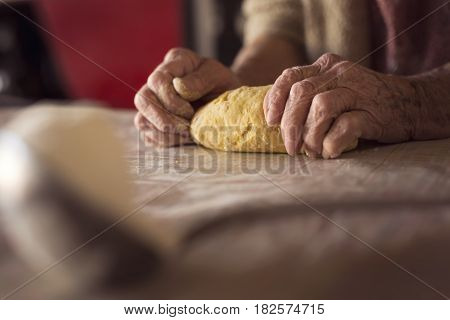 Detail of an elderly woman's hand kneading dough while making homemade pasta. Selective focus