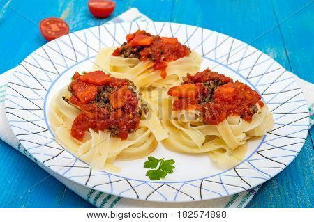 Pasta nest tagliatelle with bolognese sauce and vegetables on a plate.