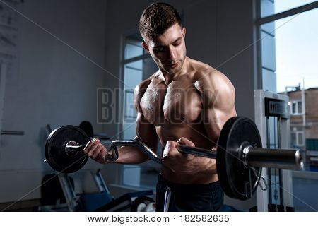 Young muscular man in shorts with a barbell trains in the gym close-up