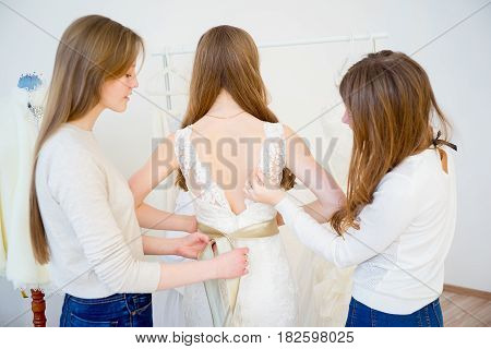 Bride trying on wedding dress with sales assistant