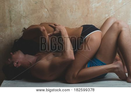 young couple of handsome macho man in blue pants with muscular body and pretty woman or sexy girl with naked chest on textured wall background laying on table