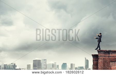 Businessman with blindfolder on eyes walking on building top
