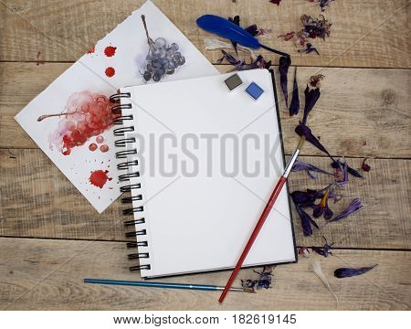 A blank sheet of paper for text surrounded by dried flower petals on a wooden background. Illustration of a hobby, drawing and inspiration. Top view.Easel, brushes, watercolor paint