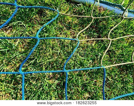 Detail of yellow blue crossed soccer nets soccer football in goal net with grass on outdoor playground in the background.