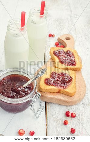 Toasts with strawberry jam and milk for breakfast on white rusric wooden background. Selective focus.