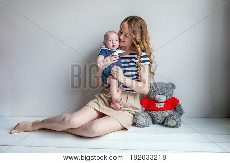 Young mother holding her newborn child. Mom nursing baby. Woman and new born boy relax in a white bedroom. Mother breast feeding baby. Family at home