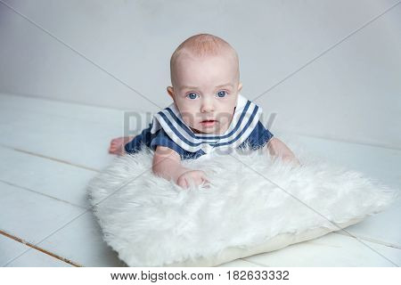 Infant child baby boy In a sailor's suit lies on his stomach on a white pillow against a white wall background