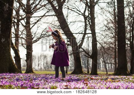Little girl with banny ears peeping from behind a tree in the park