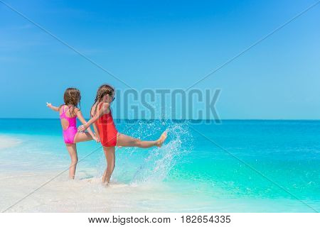 Little girls having fun at tropical beach during summer vacation playing together at shallow water