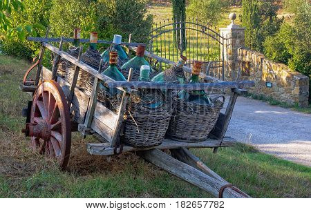 An old cart with demijohns in front of an iron gate - Montalcino, Italy
