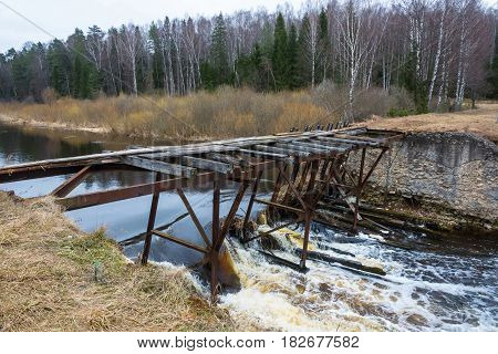 The dilapidated bridge over the small tumultuous river on a cloudy April day.
