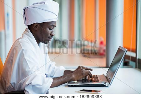 Sudanese business man in traditional outfit using mobile phone in office.