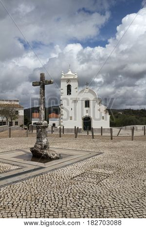 Cross and church in the main square of Querenca Portugal