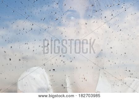 Portrait of a sad woman behind the window glass. Rainy weather