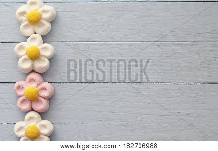 A border of pink and white marshmallow daisies on duck egg blue painted wooden table, sweet treat