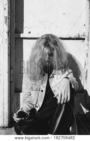 Beautiful young girl sits on the ground outdoors against the old wall background