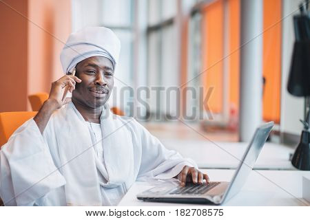 Sudanese business man in traditional outfit using mobile phone in office.