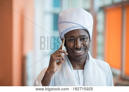 Sudanese business man in traditional outfit using mobile phone in office.
