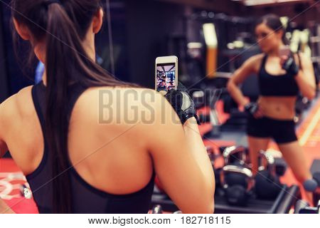 sport, fitness, lifestyle, technology and people concept - young woman with smartphone taking mirror selfie in gym