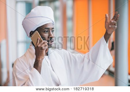 Sudanese business man in traditional outfit using mobile phone in office.