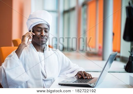 Sudanese business man in traditional outfit using mobile phone in office.