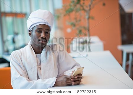 Sudanese business man in traditional outfit using mobile phone in office.