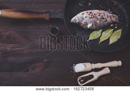 Fresh crucian in a frying pan with pepper and salt in a black frying pan top view vintage toning