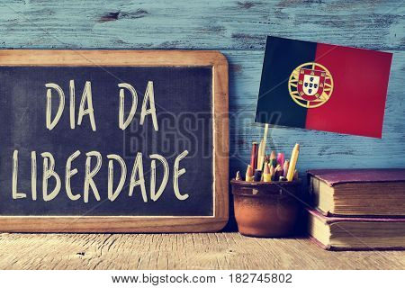 the text Dia da Liberdade, the Day of Freedom national holiday in Portugal written in Portuguese in a chalkboard, and a flag of Portugal, on a rustic wooden table
