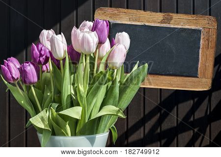 Wooden chalkboard copyspace Sign with beautiful pinktulips bucket spring flowers tulip brown background