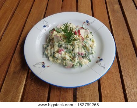 Delicious spring salad with eggs, radishes, spinach, parsley, green onions, dill, mayonnaise, made at home. The plate is on a wooden table. Suitable for design sites and magazines on cooking