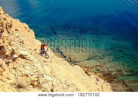 Mountain biker riding on bike in summer inspirational mountains and sea landscape. Man cycling MTB on enduro trail track at seaside and rocky dirt path. Sport fitness motivation and inspiration.