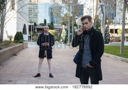 Two young business men on the street talking on the mobile phone. They wear modern and stylish clothes.
