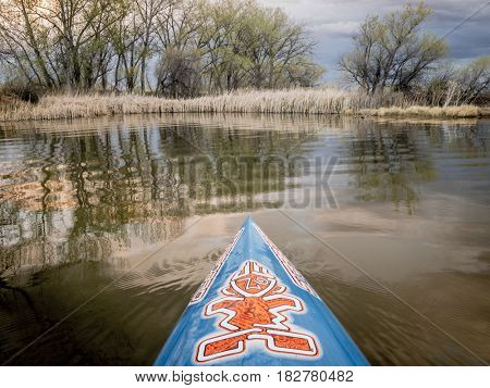 FORT COLLINS, CO - April 19, 2017:  Paddling a stand up paddleboard by Starboard  on a small lake with early spring lake scenery.