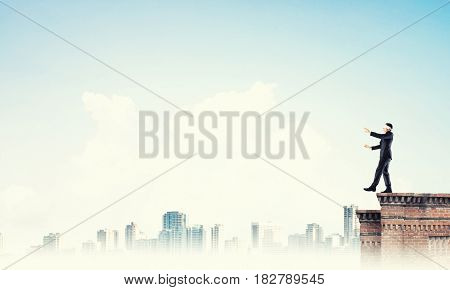 Businessman with blindfolder on eyes walking on building top