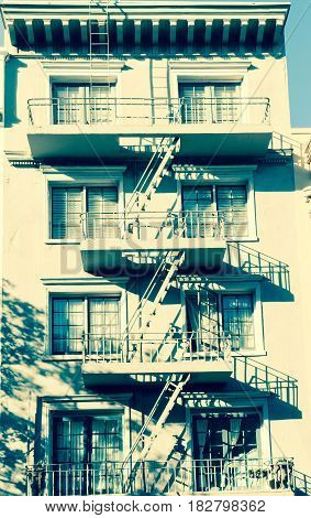 Retro styled image four storey building with characteristic old city with shadows of fire escape ladders connecting balconies to the ground San Francisco USA.