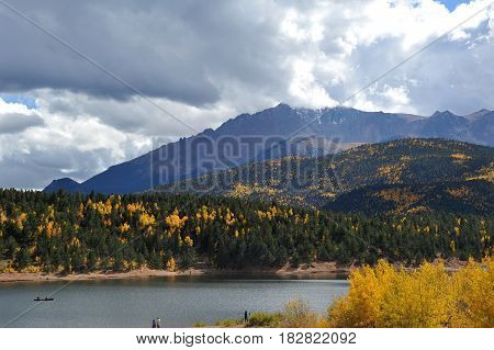 A view of Pikes Peak crested with snow and surrounded by storm clouds as seen from below behind Cyrstal Resevoir.