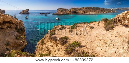 Comino Malta - The beautiful Blue Lagoon with turquoise clear sea water yachts and snorkeling tourists on a sunny summer day with the island of Gozo at background