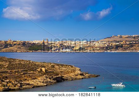 Comino Malta - Motorboat and yacht at the famous Blue Lagoon on the island of Comino with Gozo and Mgarr town at the background on a bright sunny summer day