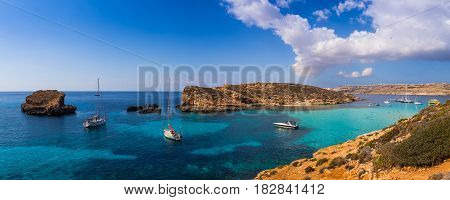 Comino Malta - Panoramic skyline view of the famous and beautiful Blue Lagoon on the island of Comino with sailboats traditional Luzzu boats and tourists enjoying the azure mediterranean sea water and sunshine