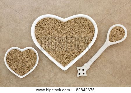 Teff super grain health food in heart shaped porcelain dishes and spoon on hemp paper background.