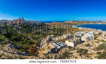Il-Mellieha Malta - Beautiful panoramic skyline view of Mellieha town on a bright summer day with Paris Church Agatha Red Tower and Mellieha beach at background with blue sky and clouds