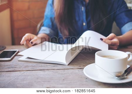 A woman opening and reading a book with coffee cup on wooden table in vintage cafe