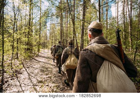 Group Of Re-enactors Dressed As Soviet Russian Red Army Infantry Soldiers Of World War II Marching Along Forest Road At Spring Season.