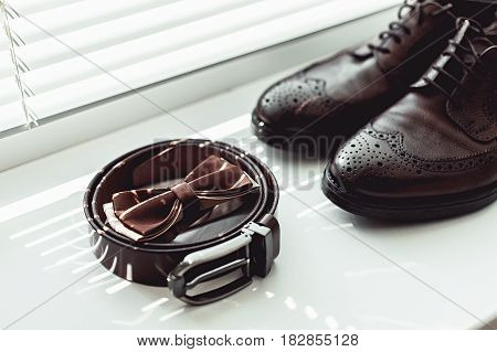 Brown bow tie, leather shoes and belt. Grooms wedding morning. Close up of modern man accessories on the window sills with shutters. Look from above