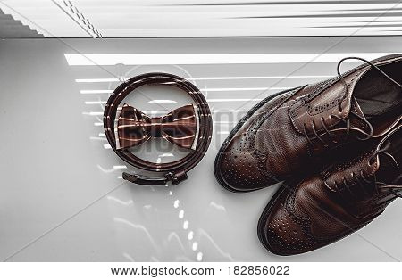 Brown bow tie, leather shoes and belt. Grooms wedding morning. Close up of modern man accessories on the window sills with shutters. Look from above