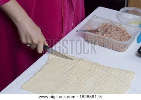 Stages Of Preparation Of Meat Glomeruli. A Woman Slices Thin Strips Of Dough. Next To The Table Is A