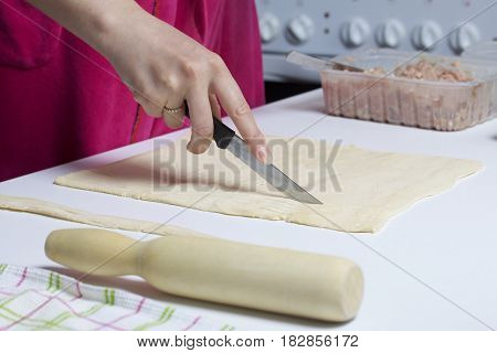 Stages Of Preparation Of Meat Glomeruli. A Woman Slices Thin Strips Of Dough. Next To The Table Is A