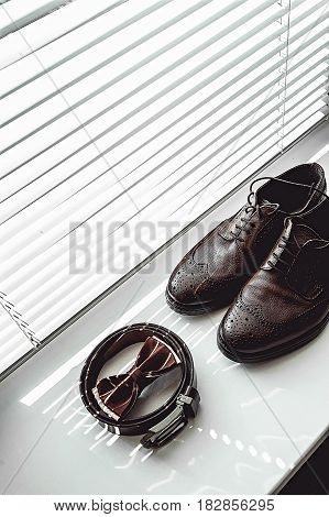 Brown bow tie, leather shoes and belt. Grooms wedding morning. Close up of modern man accessories on the window sills with shutters. Look from above