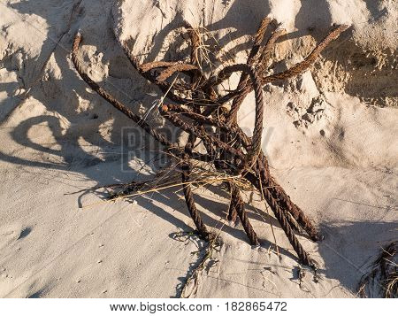 metal wire that is weathered lies half buried in the sand at the beach